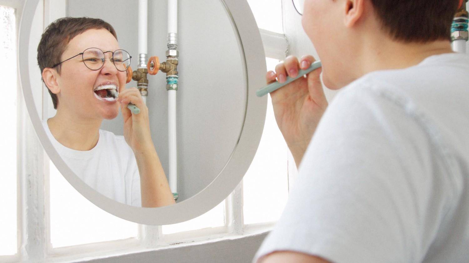 caucasian-woman-with-short-haircut-front-mirror-bathroom-full-sunlight-brush-her-teeth (2) Adult brushing teeth for daily oral hygiene
