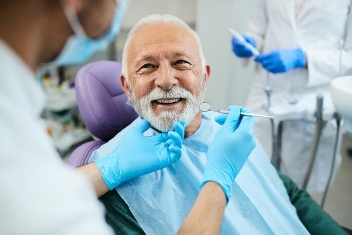 Invisalign Smiling elderly man undergoing a dental checkup while a dentist uses tools to examine his teeth in a modern clinic.
