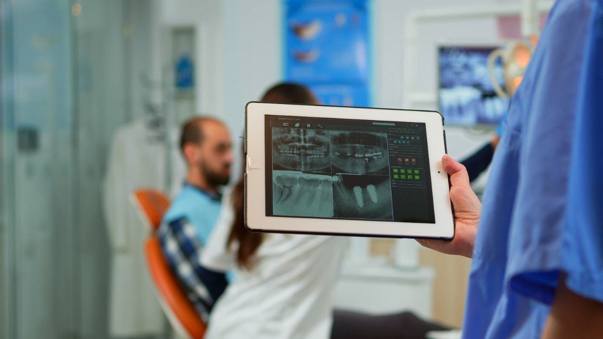 natural-tooth-root-canal-treatment Dentist showing dental X-rays on tablet to patient