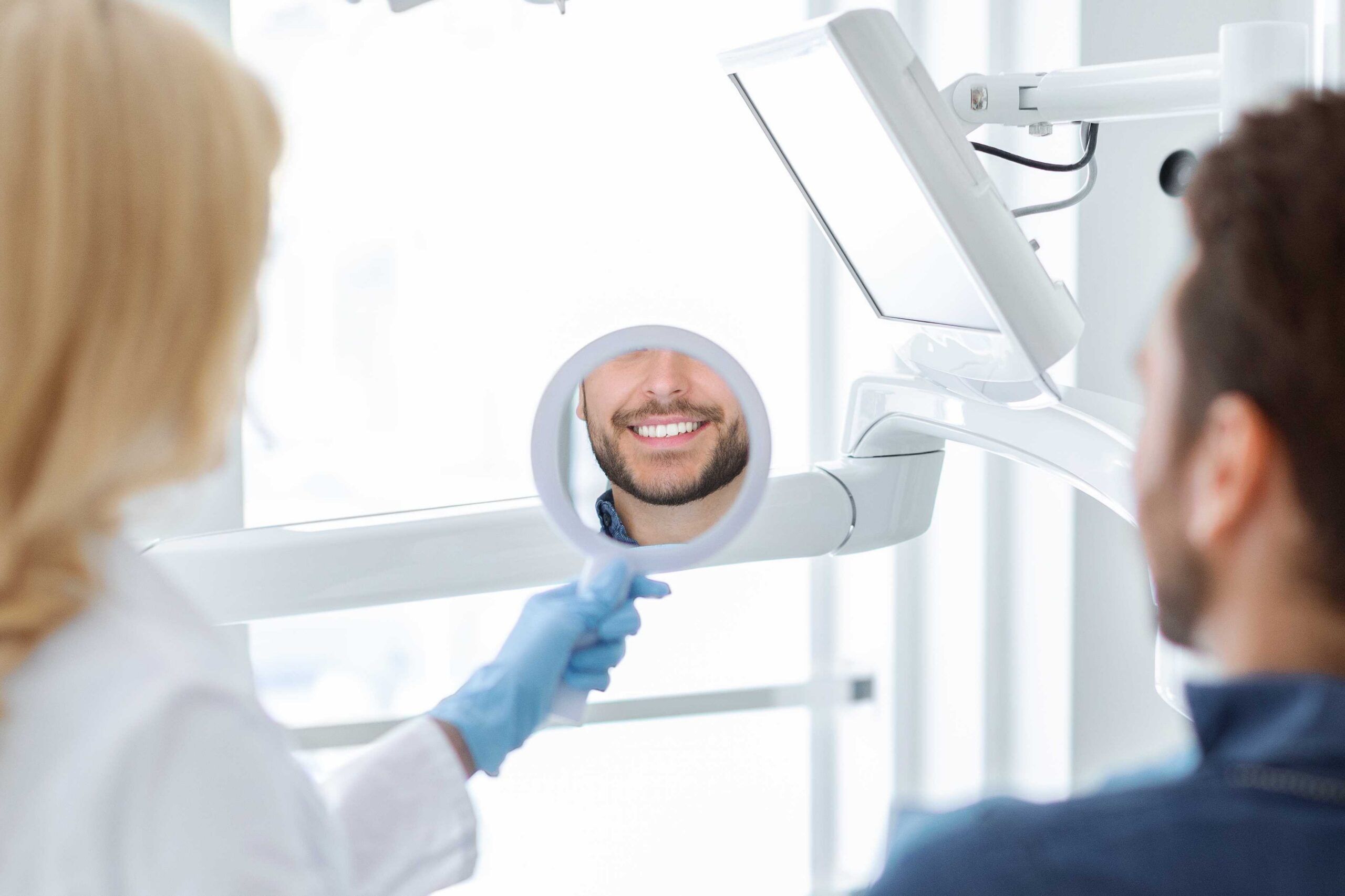 Dentist holding a dental mirror while a patient shows a bright smile.