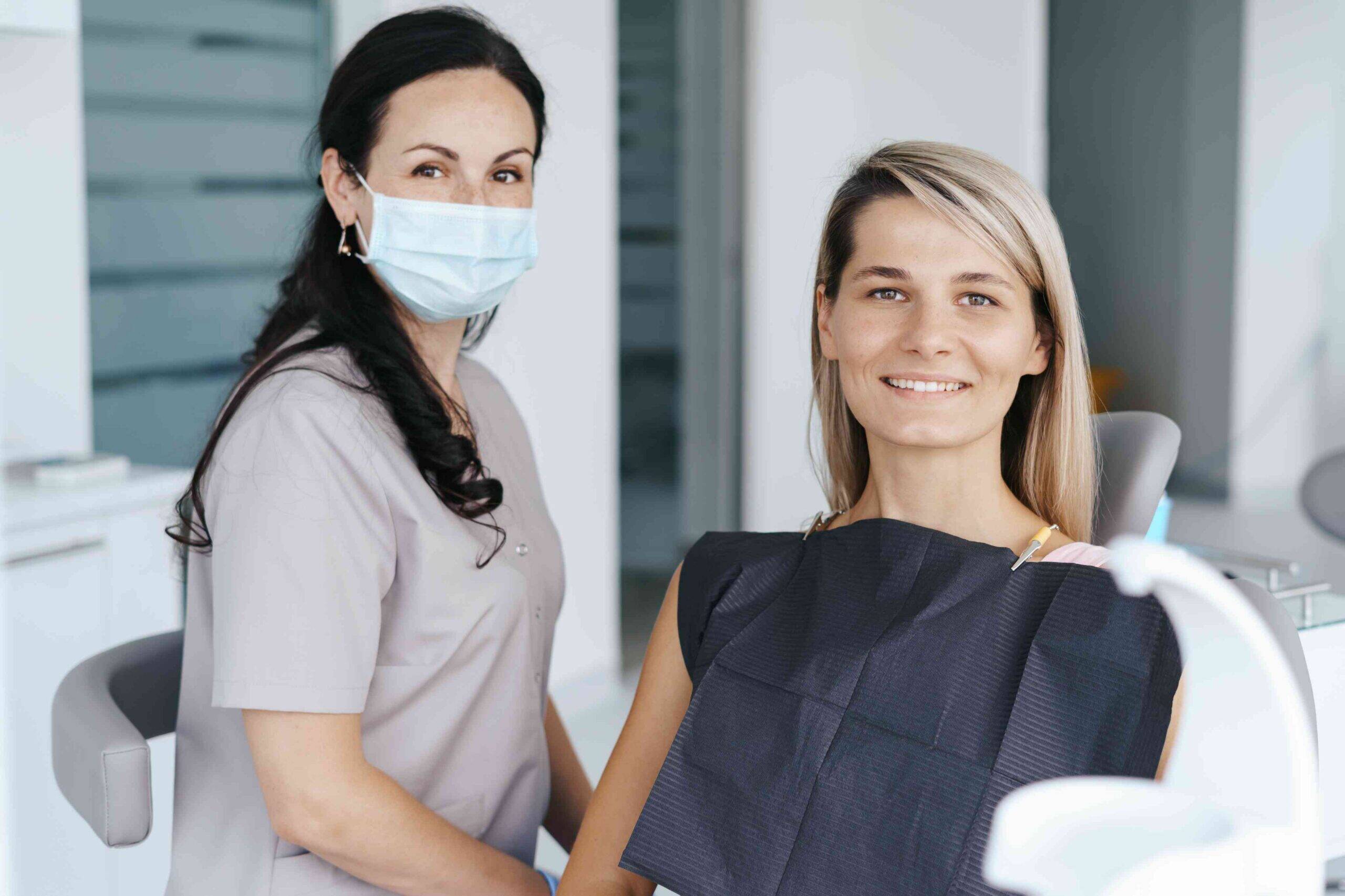 cosmetic-dentist-smile-health Dentist sitting beside a smiling patient in a dental chair during a routine dental examination.