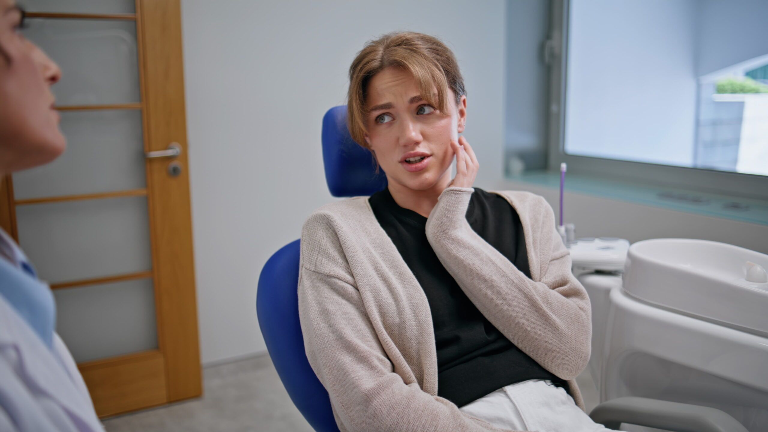 Patient complaining dental pain in stomatology clinic closeup. Woman dentist Patient experiencing jaw discomfort during a dental consultation
